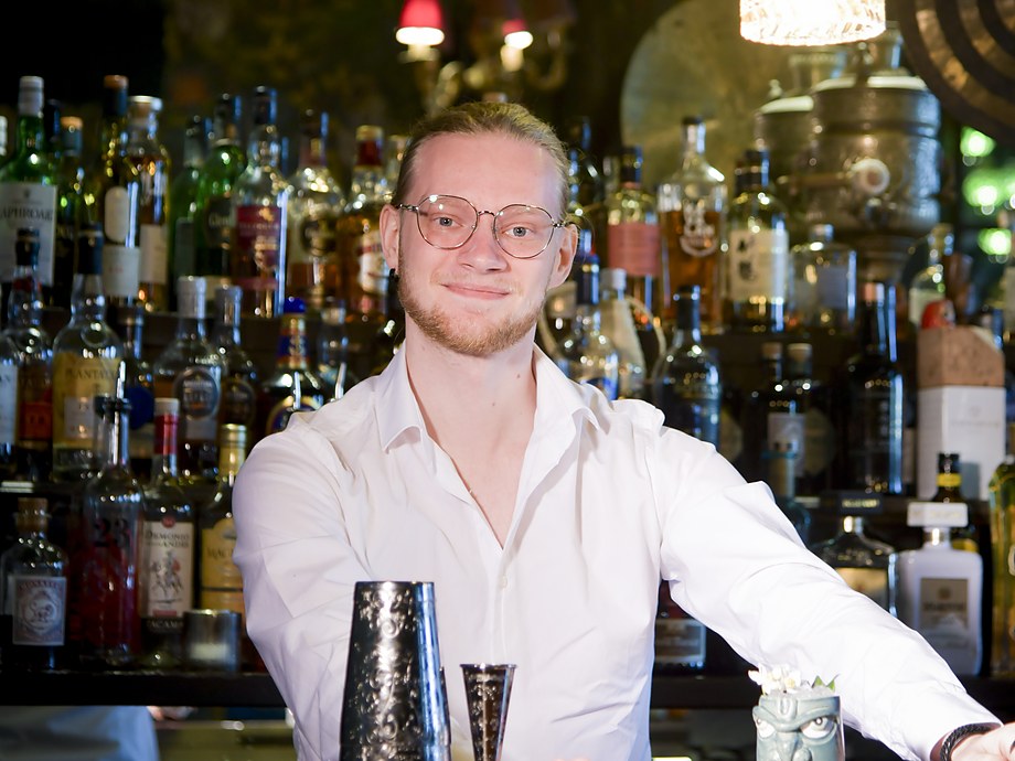 Flemming Mallant en chemise blanche derrière un bar, un shaker et un verre à mesurer posés devant lui