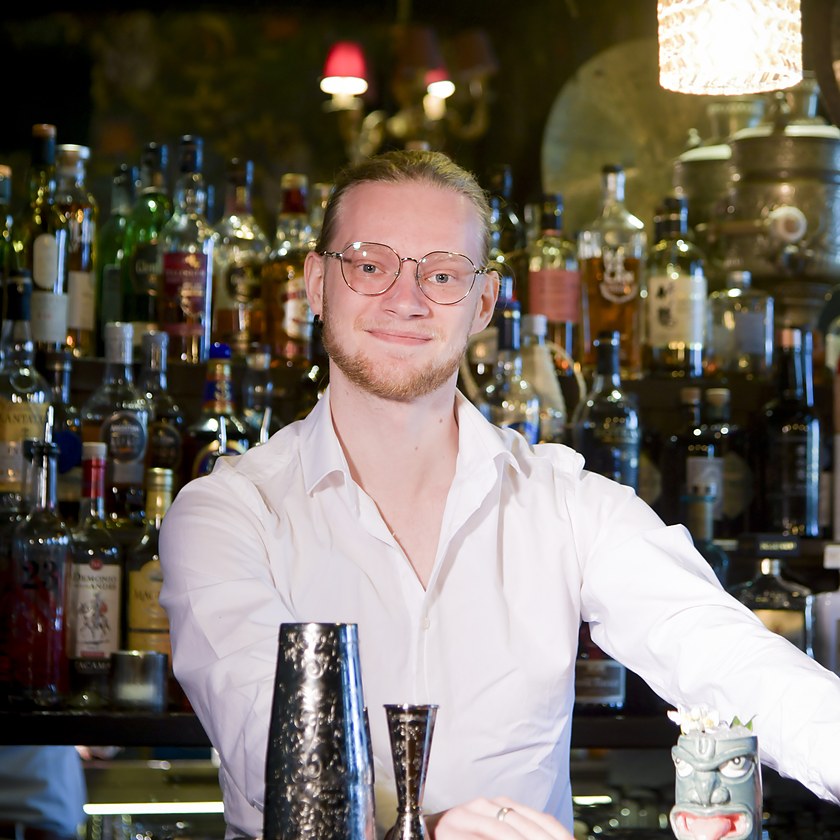 Flemming Mallant derrière son bar, devant les bouteilles, shaker et mug tiki à portée de main